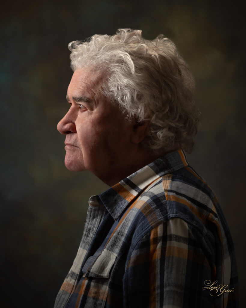 A man with white hair and plaid shirt looking to his left.